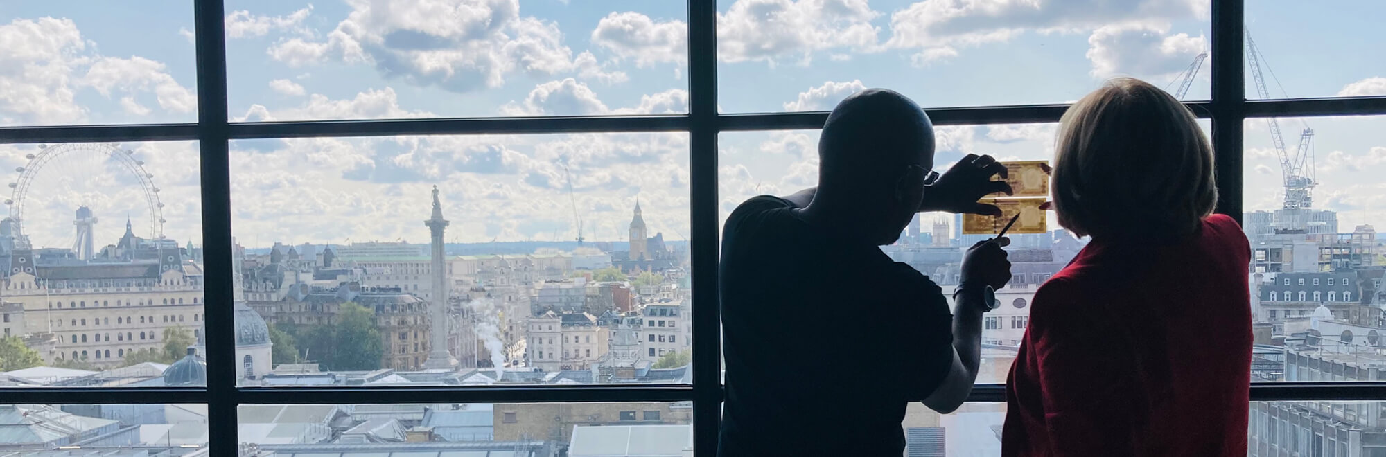 two colleagues hold a bank note against a window to see the authentication features
