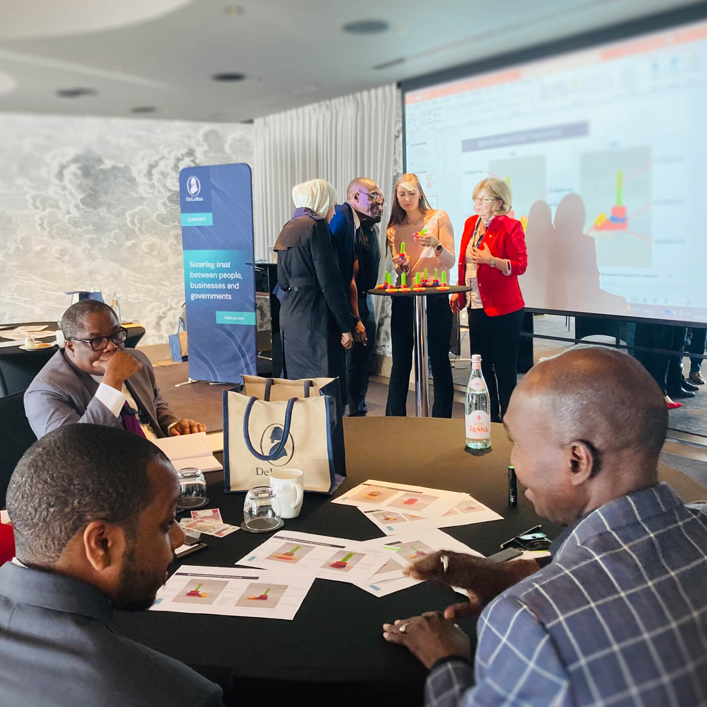 a group of currency professionals gather in front of a presentation in a modern board room