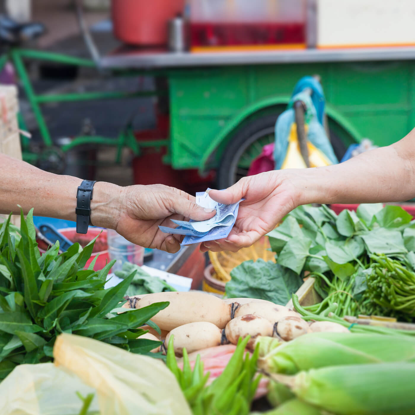 two people exchanging bank notes at a vegetable market stall