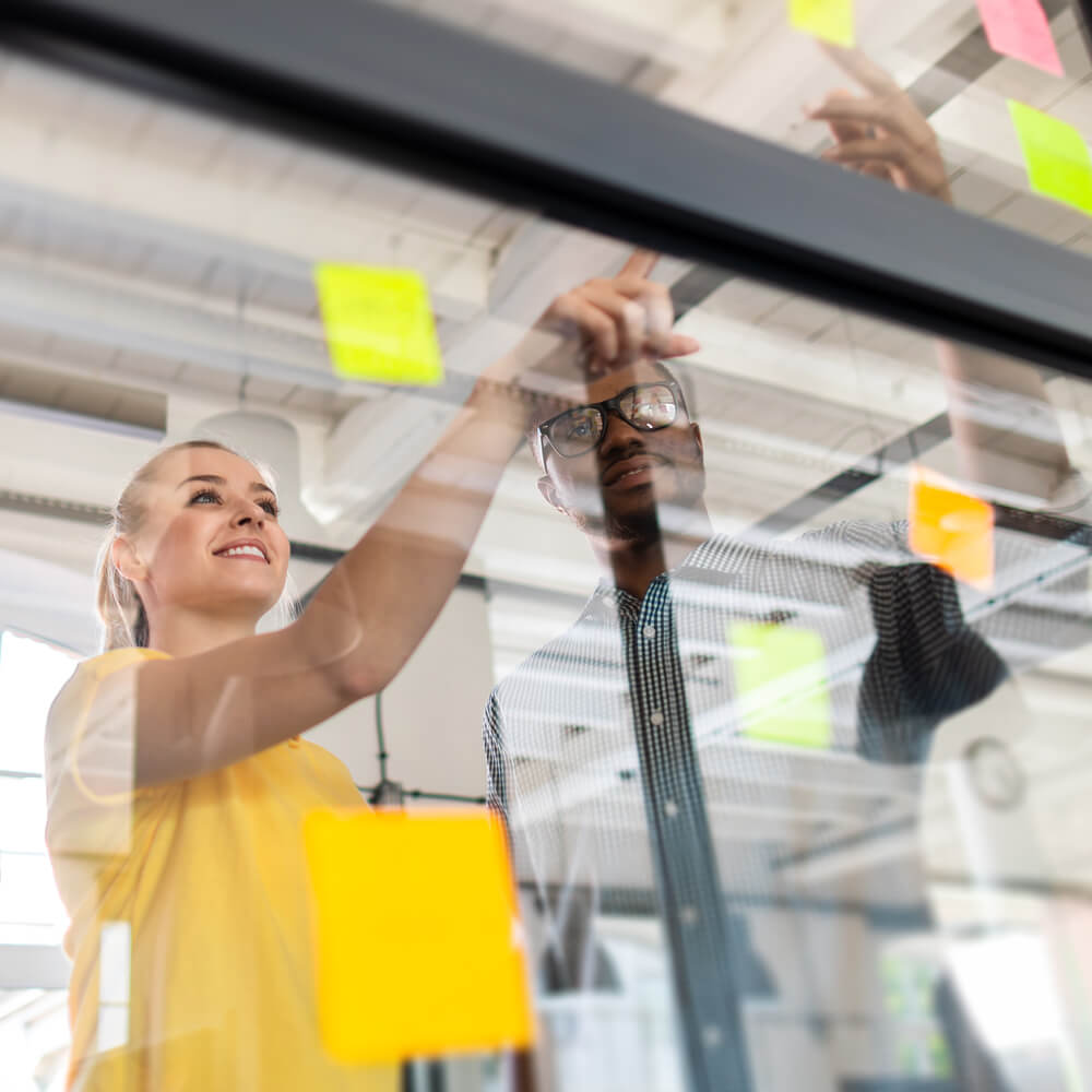 a male and female coworker gather around a window of post-it notes