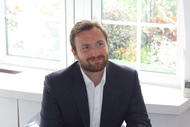 a photo of Ben Crosland (Senior Communications Adviser at De La Rue PLC) smiling at the camera in a modern and bright office space
