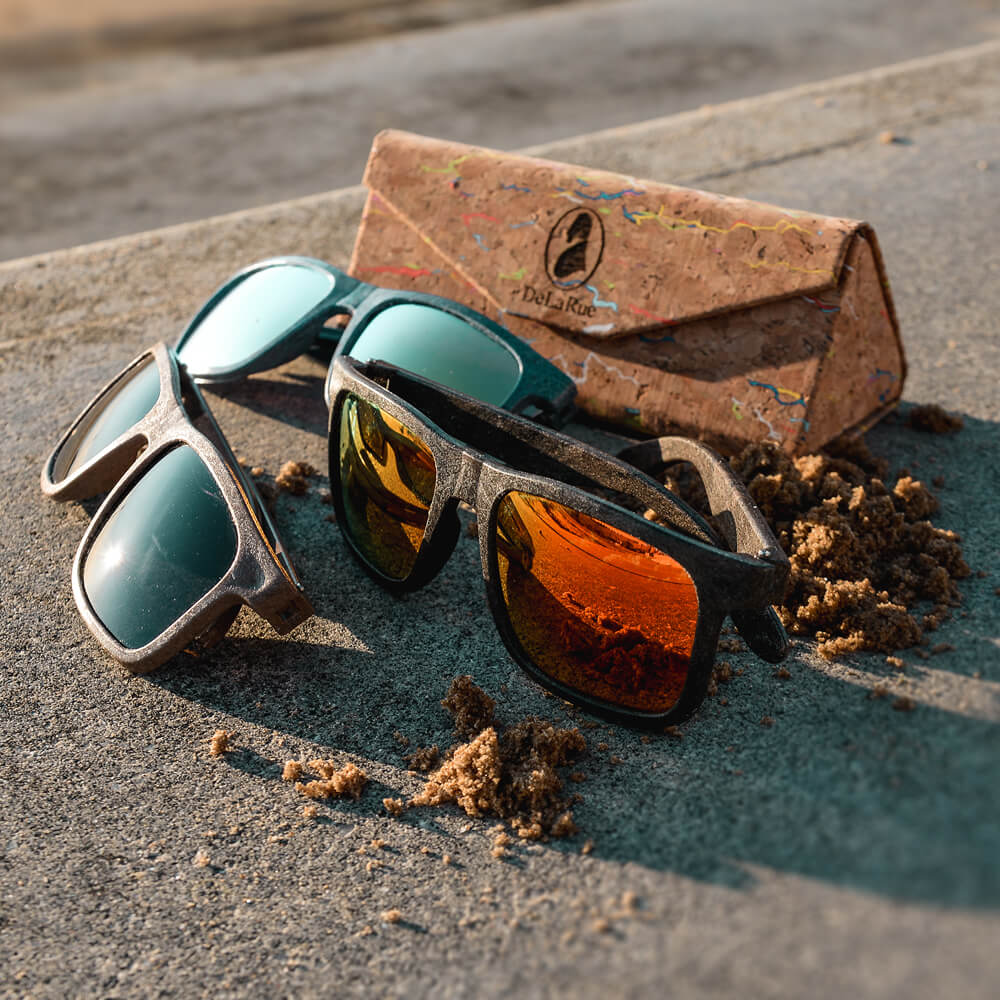 a collection of sunglasses sitting on a beach wall with a cork sunglasses case in the background
